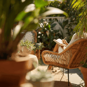 A calm, sunny backyard with a person journaling in a chair with plants nearby, symbolizing mindful moments, intention, and self-care during summer.